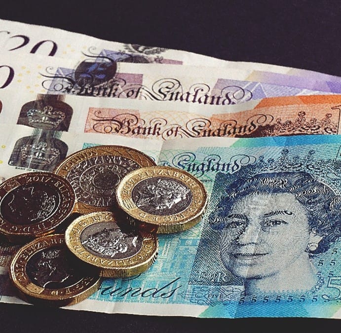 Assorted Bank of England banknotes in multicolored hues featuring a portrait of Queen Elizabeth II, with British coins scattered on a dark surface